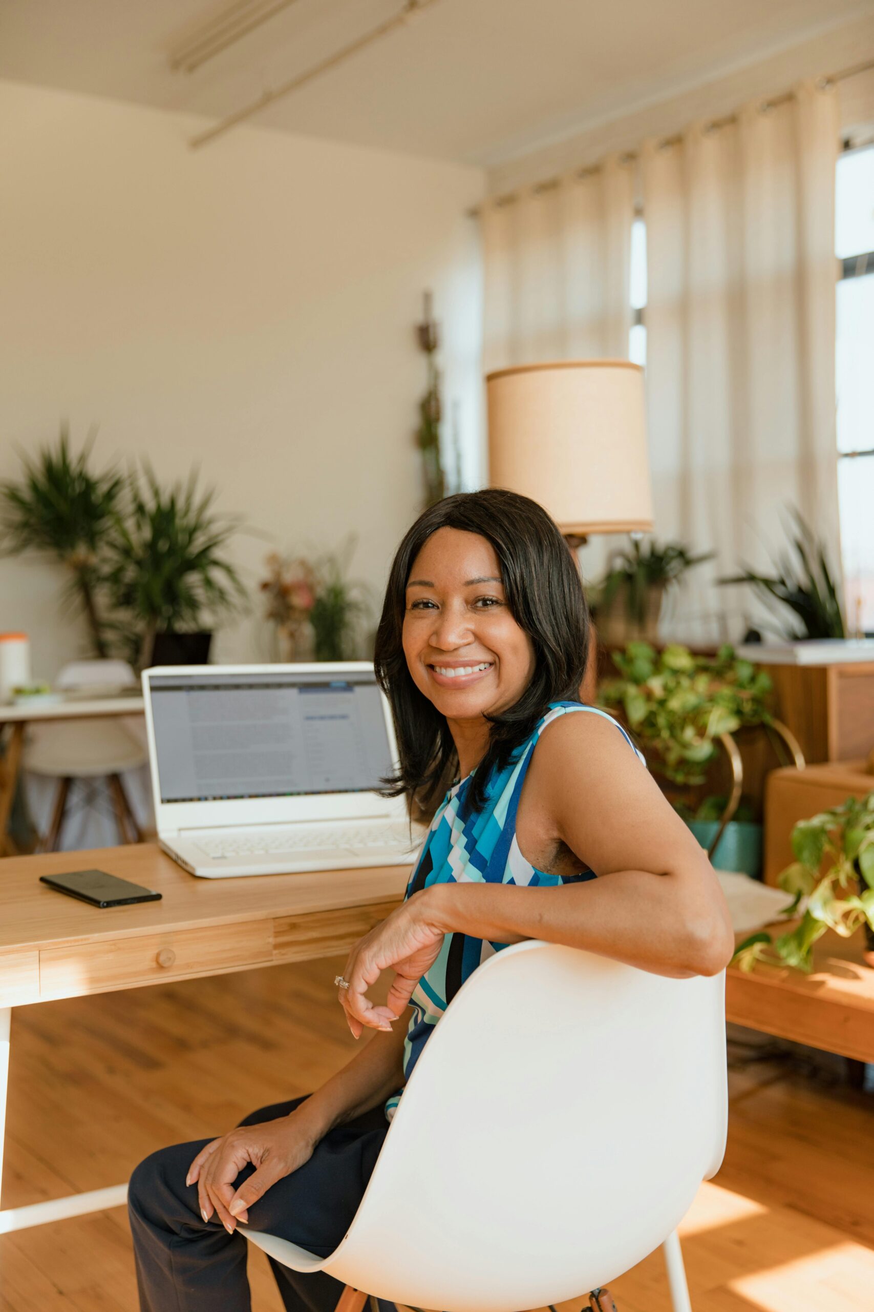 Smiling woman working on a laptop in a bright, plant-filled office setting.
